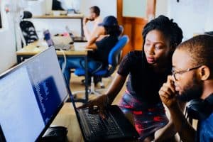 Two colleagues sit right of frame, one indicating towards a computer screen. They are in the process of automating content governance.