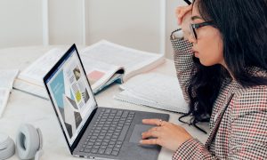 A woman views her open laptop, the screen visible to us.