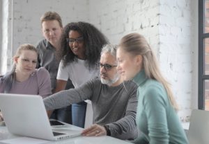 Five people gather around a laptop smiling as one of them points to the screen.