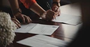 Multiple sets of hands are signing documents spread out on a table.