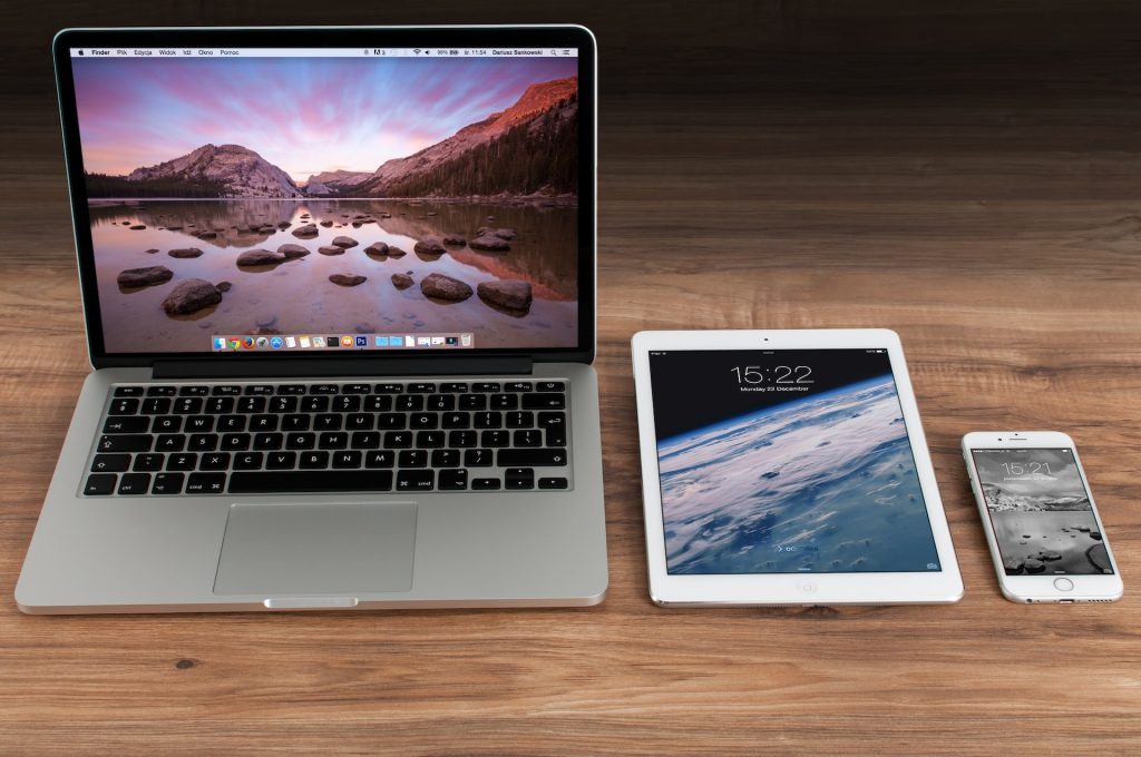 From left to right on a timber desk: A macbook laptop, an iPad, an iPhone