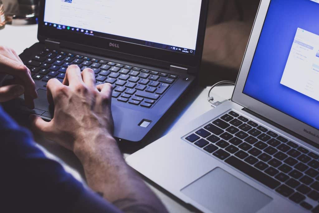 A close up of two open laptops side by side, a man's hands on the left keyboard.