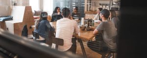 A group of people sit casually around a desk in an office.