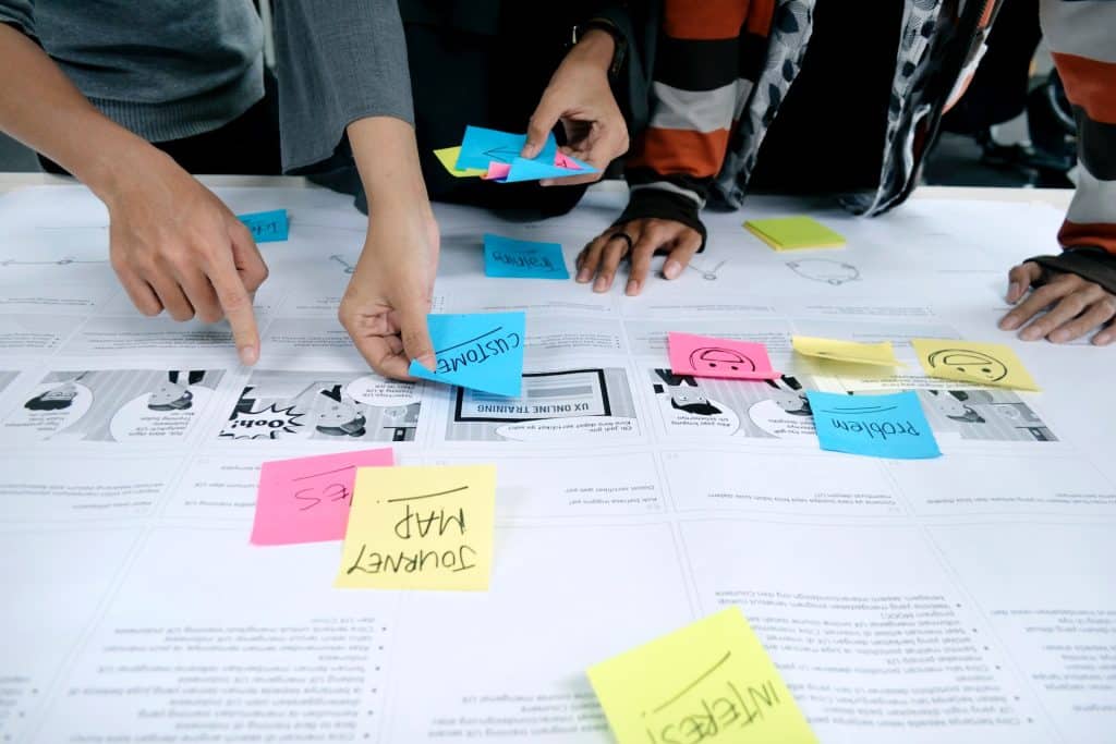 Papers and post-it notes are spread across a desk. Several people are gathered, pointing and planning.