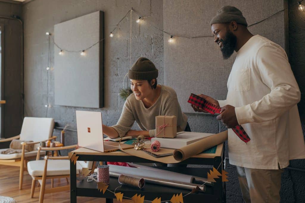 Two people stand at a tall desk in a fun office, smiling at their Microsoft laptops