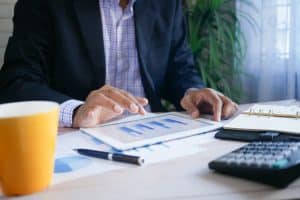 A close up shot of a man in business attire sitting at a table, his hands poised over a smart tablet that has graphs on it. It shows that Microsoft 365 for business intelligence can be used by anyone.