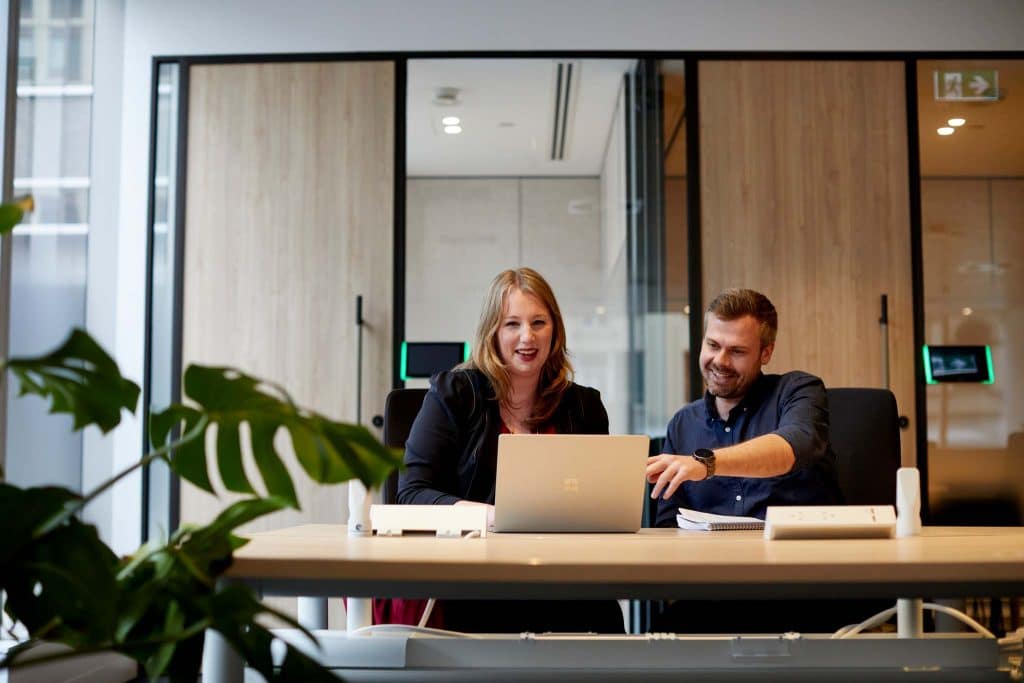 Two Propelle staff sit side by side at a desk, smiling at a laptop.