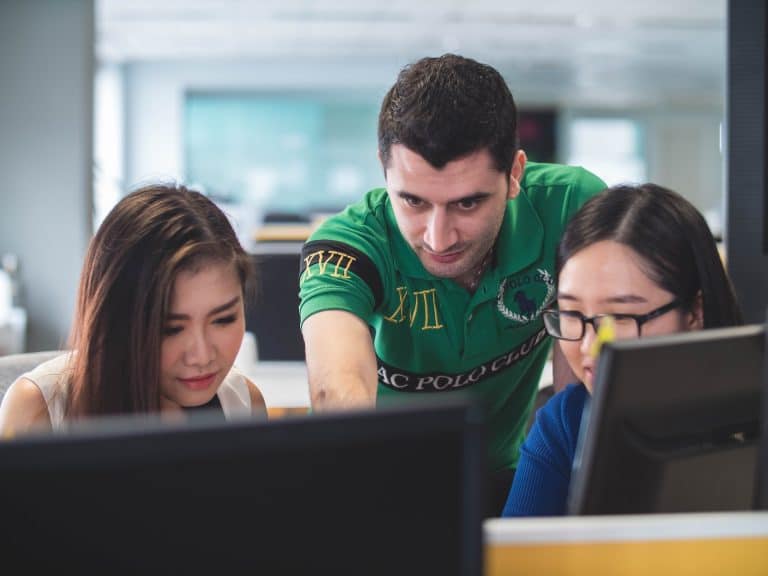 Two women and a man look towards the camera, their eyes on the computers in front of them.