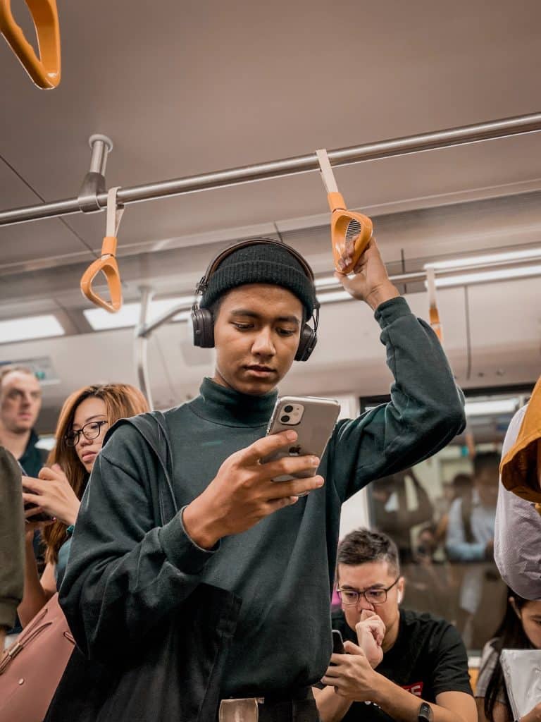 A person stands on a packed train, looking down at their smartphone.