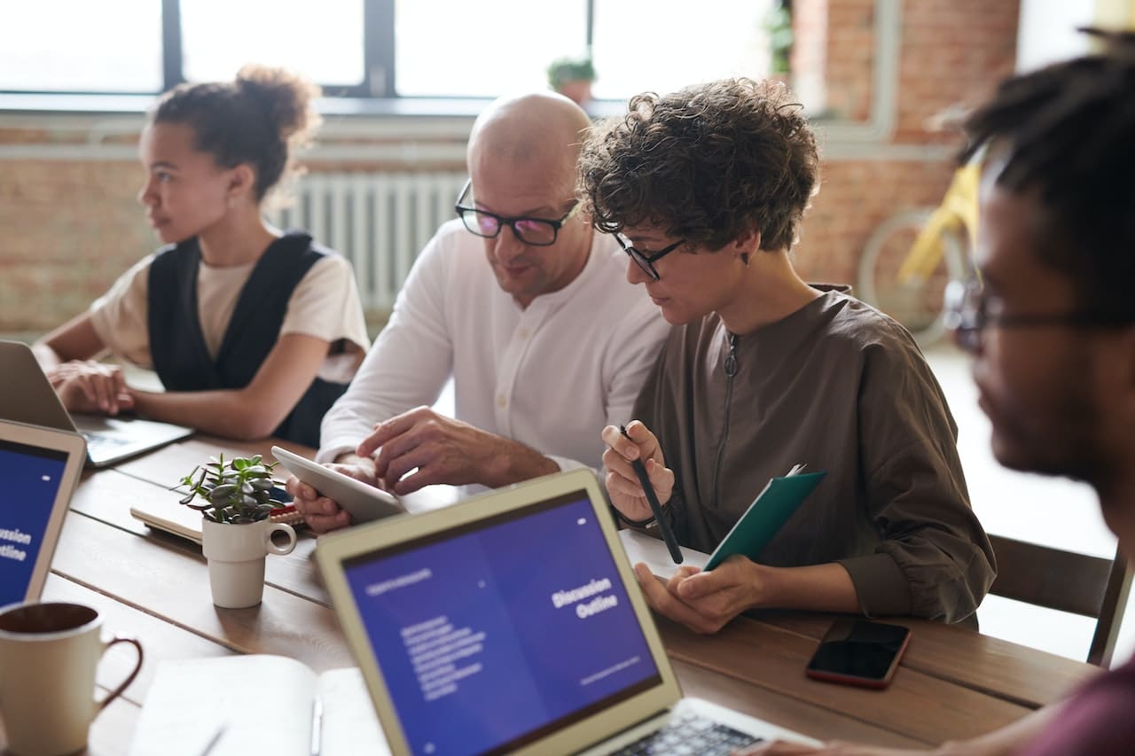 A team gathered around a conference table in a light office, laptops open, discussions in progress
