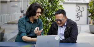 Two men sit side by side discussing Power Bi visualisation tricks at an outdoor table with a laptop