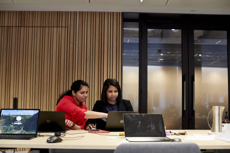 Two women working side-by-side on laptops to set up SharePoint Online