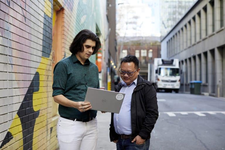 Two men standing in city laneway looking at a laptop showing what makes a great SharePoint intranet