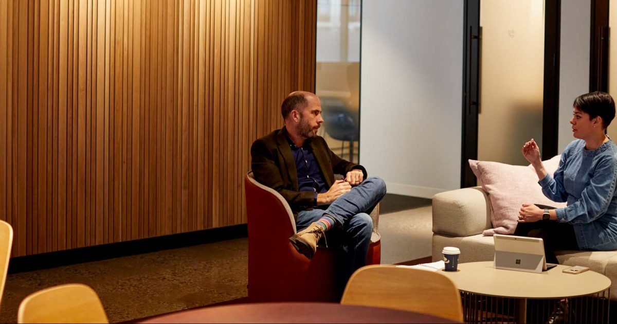 A man and a woman sit around a low coffee table, discussing file naming conventions