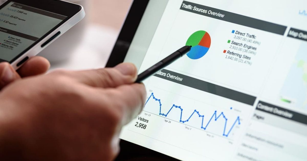 A laptop with a variety of charts and figures, a pen points at a pie chart on the screen.