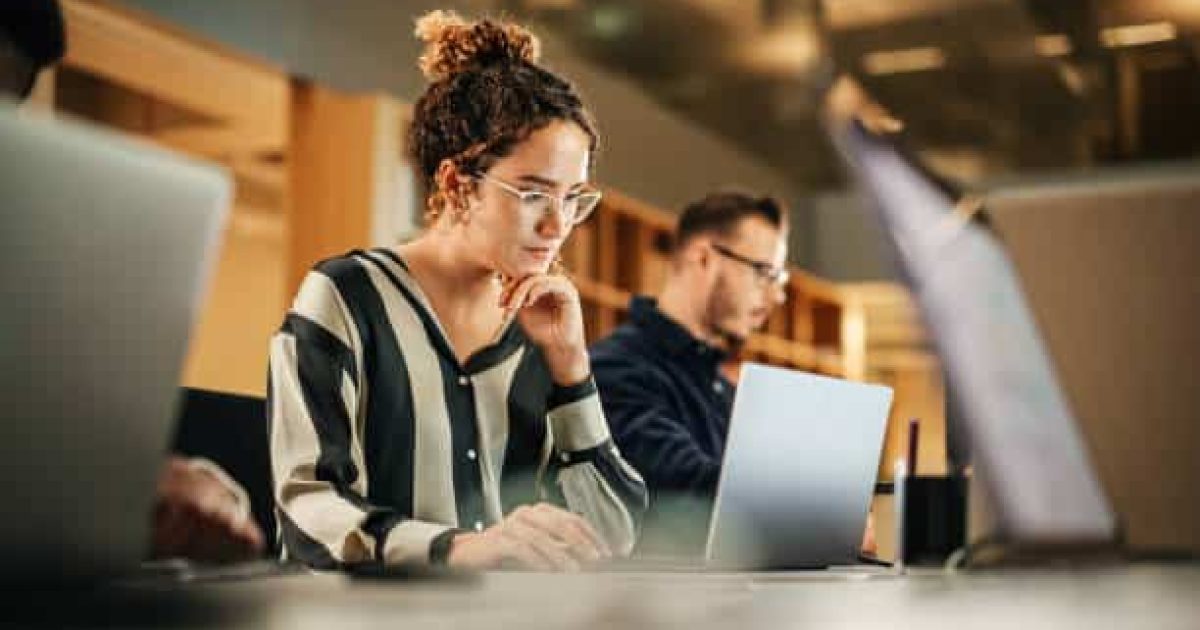 Portrait of Enthusiastic Hispanic Young Woman Working on Computer in a Modern Bright Office. Confident Human Resources Agent Smiling Happily While Collaborating Online with Colleagues.