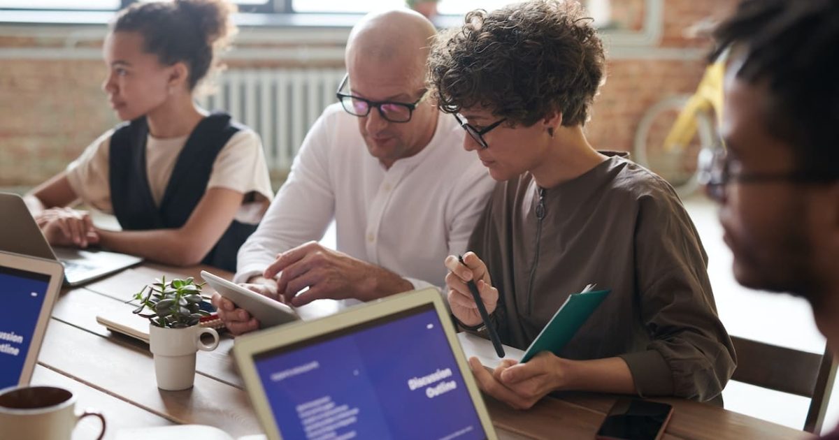 A team gathered around a conference table in a light office, laptops open, discussions in progress