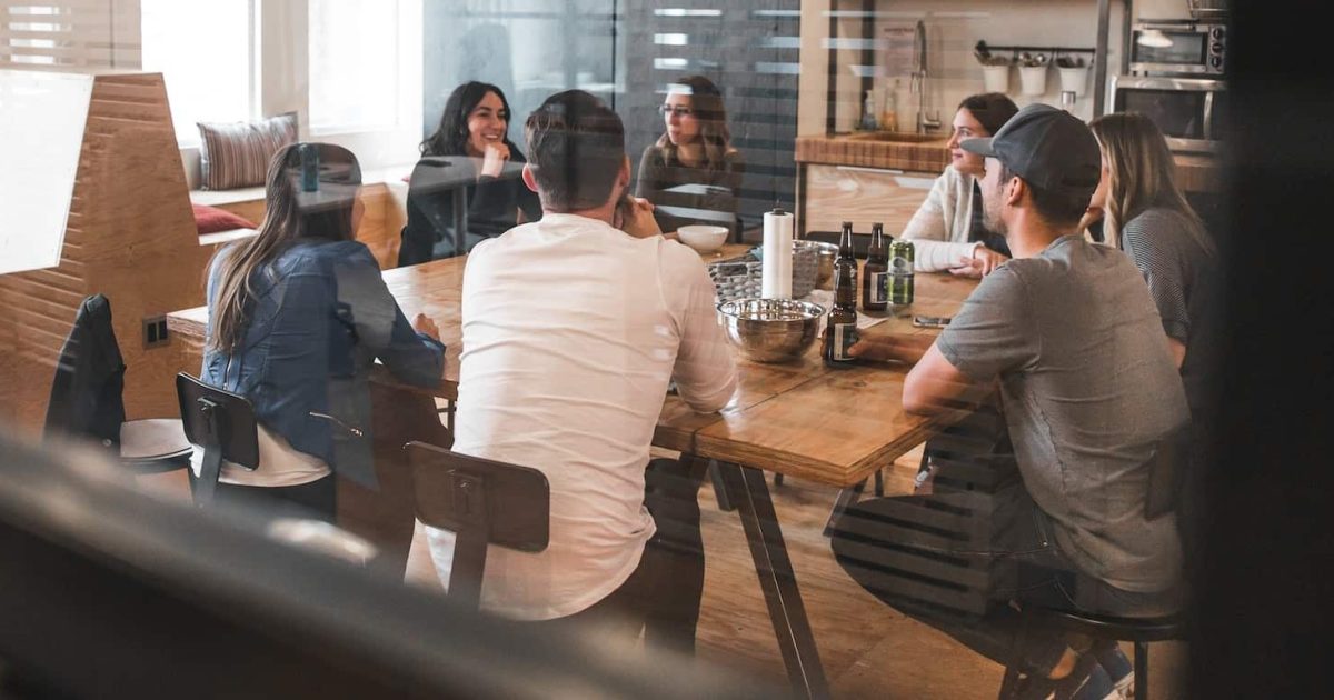 A group of people sit casually around a desk in an office.