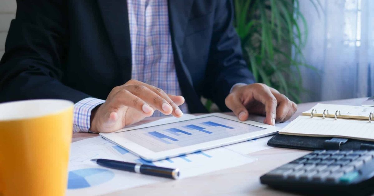 A close up shot of a man in business attire sitting at a table, his hands poised over a smart tablet that has graphs on it. It shows that Microsoft 365 for business intelligence can be used by anyone.
