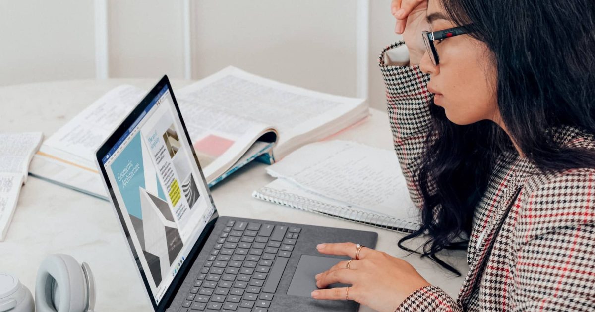 A woman views her open laptop, the screen visible to us.