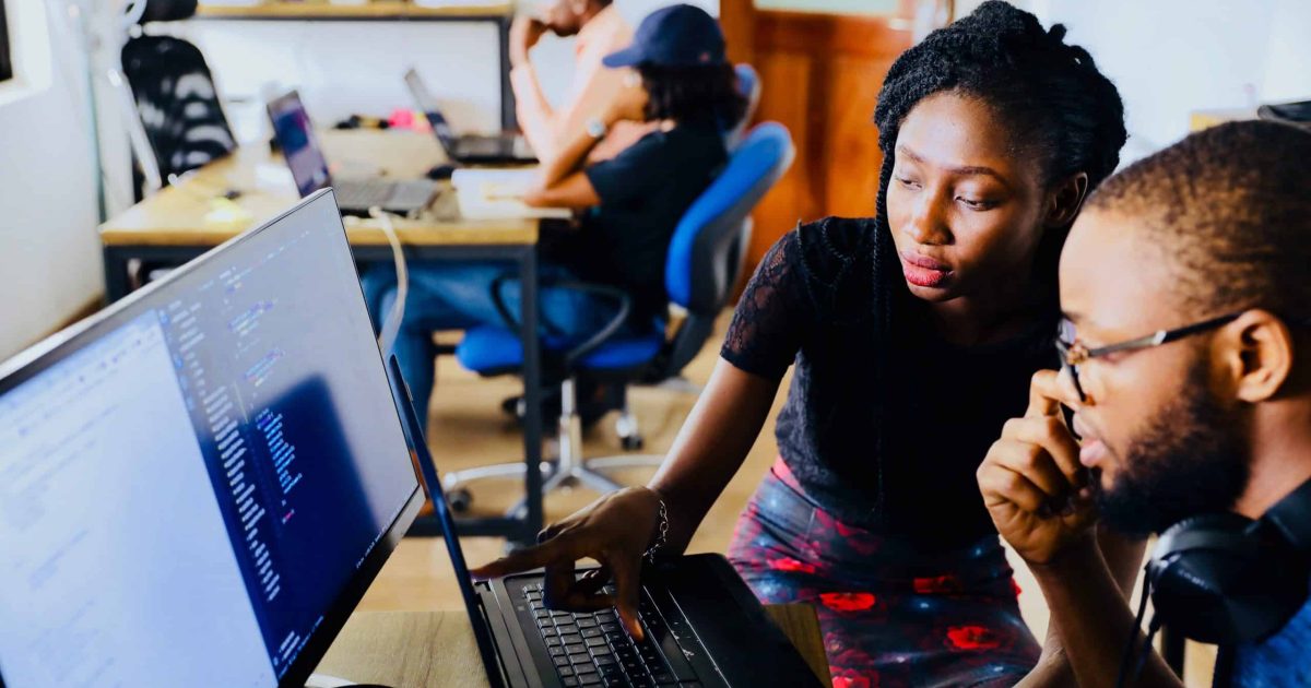 Two colleagues sit right of frame, one indicating towards a computer screen. They are in the process of automating content governance.